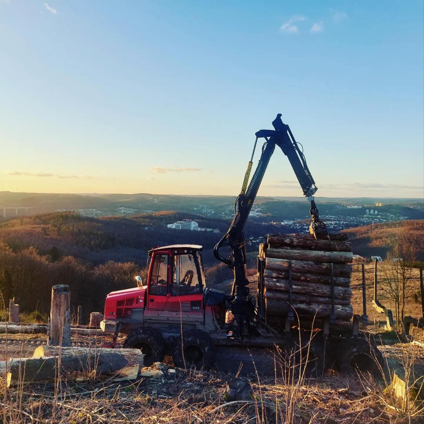 Roter Komatsu-Rückezug mit Holz bei Sonnenuntergang, Blick über das Siegerland