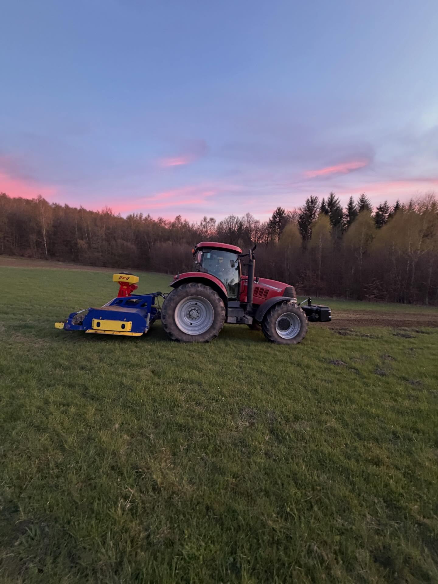 Schlepper mit Kreiselegge und Sämaschine auf Grünland in der Abenddämmerung